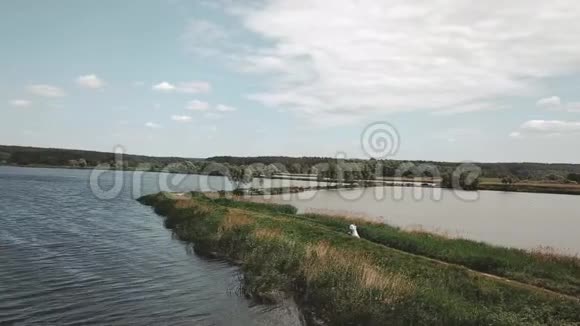 新娘和新郎在婚礼当天有浪漫的散步夫妇沿着湖边的小路散步空中拍摄视频的预览图