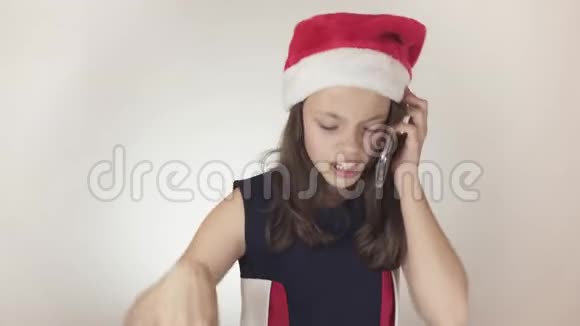 戴着圣诞老人帽子的漂亮顽皮少女在白色背景下的智能手机上进行情感交流视频的预览图