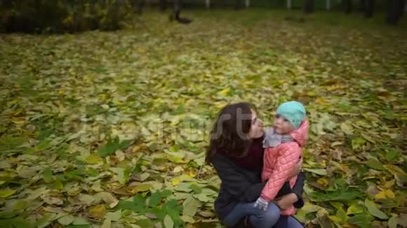 妈妈带着孩子在秋天公园快乐的年轻妈妈和小女孩在秋天的森林里休息慢动作视频的预览图