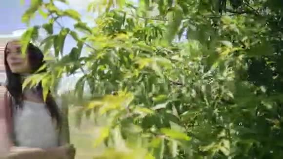 一个年轻漂亮的女人靠近满是树枝的绿树视频的预览图