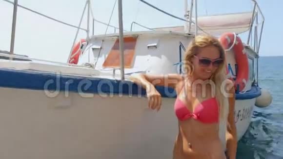 戴墨镜的金发碧眼在沙滩上的船边摆着粉色比基尼视频的预览图