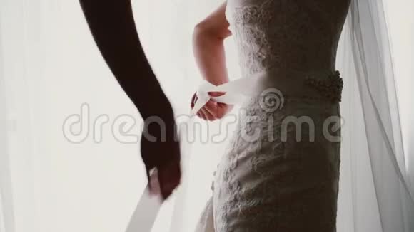 年轻新娘的近景在她的婚纱上鞠躬女人站在窗前穿上西装视频的预览图