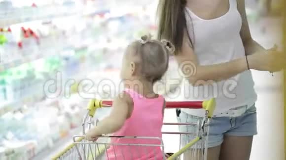 当妈妈在超市挑选商品时小女孩正坐在蹒跚学步的孩子身上视频的预览图
