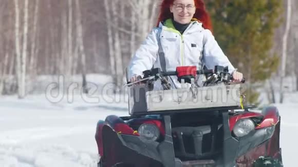 一个满脸笑容的姜黄色头发的女人在森林里骑雪地车视频的预览图