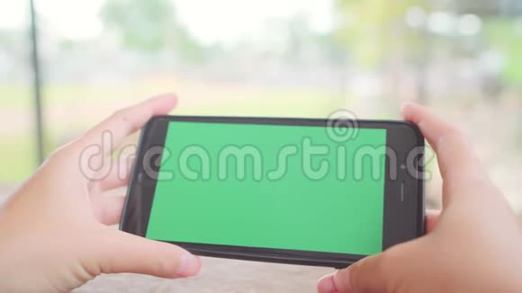 年轻的亚洲女性使用带有绿色屏幕的黑色手机设备亚洲女人拿着智能手机在咖啡馆里滚动页面视频的预览图