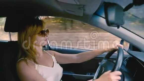 快乐美丽的金发女人戴着太阳镜开车4K慢动作视频的预览图