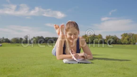 阳光明媚美丽的微笑女孩在公园草地上看书的画像视频的预览图