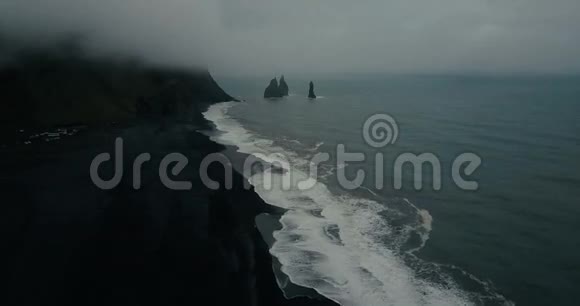 冰岛黑色火山海滩的鸟瞰图和海洋中的巨魔脚趾岩石直升机用泡沫飞过波浪视频的预览图