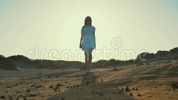 穿着白色连衣裙的女孩从日落走到相机沙漠慢动作视频的预览图