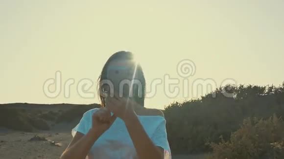 穿着白色连衣裙的女孩在日落时分在沙漠里打电话拍照夏日的黄昏清晨剪影视频的预览图