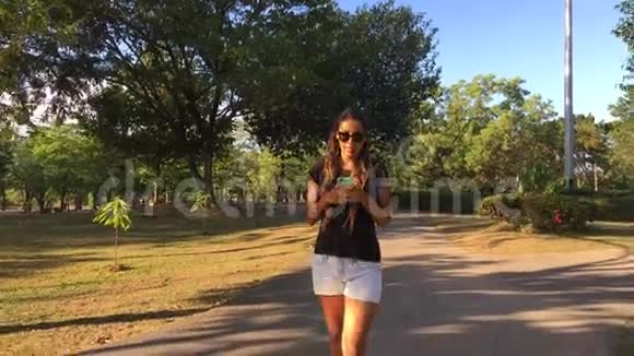 年轻女子在公园散步智能手机发短信慢镜头高清Stadicam镜头视频的预览图