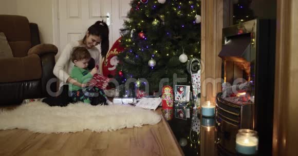美丽的年轻母亲和儿子微笑着在圣诞树附近打开礼物2016年圣诞节4K视频的预览图
