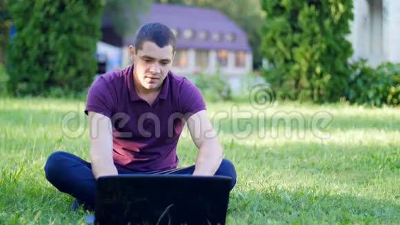 在草坪上拿着笔记本电脑工作的年轻人视频的预览图
