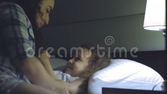 漂亮的母亲在孩子睡觉前给孩子一个前吻轻轻地拥抱孩子非常甜蜜地盖住她视频的预览图