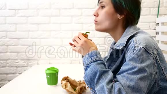 女人吃三明治坐在咖啡馆的窗户附近视频的预览图