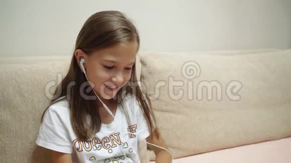 戴着耳机听音乐的小女孩坐在沙发上视频的预览图