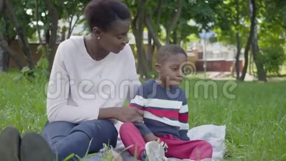 肖像漂亮的非裔美国妇女坐在毯子上她的小儿子在公园里玩玩具这就是视频的预览图