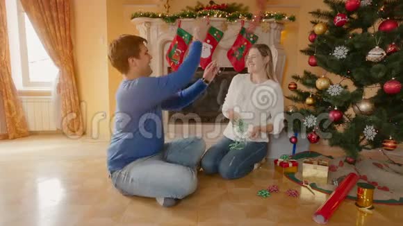 幸福的年轻夫妇坐在客厅的地板上在装饰圣诞树时玩得很开心视频的预览图