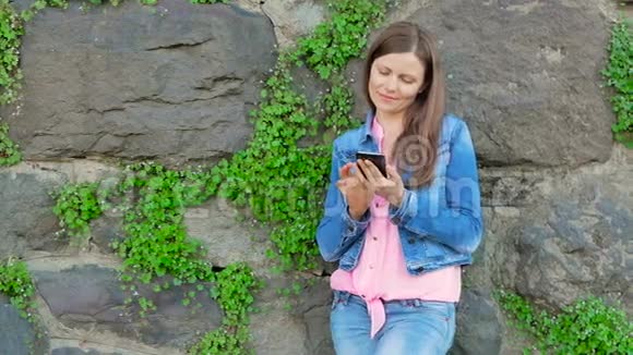 穿着棉袄用智能手机的漂亮女孩背景中野石的复古墙视频的预览图