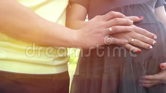 双手抚摸怀孕的肚子丈夫手抚摸着怀孕妻子的腹部柔和的夕阳照亮了视频的预览图