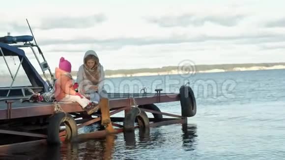 女人带着女孩妈妈带着女儿坐在桥上河边野餐穿着暖和的衣服视频的预览图