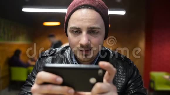 坐在咖啡馆里玩智能手机游戏的年轻人视频的预览图