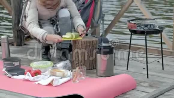 一位穿着暖和衣服的女游客背着背包在河边的一座桥上筛蔬菜准备食物视频的预览图