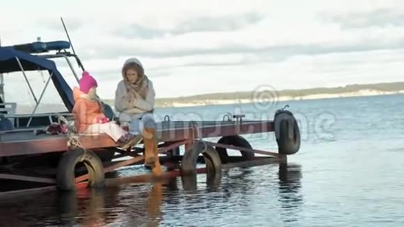 女人带着女孩妈妈带着女儿坐在桥上河边野餐穿着暖和的衣服视频的预览图