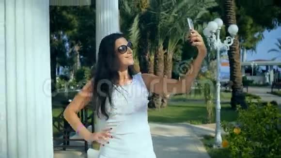 美丽快乐的年轻女人在夏天的公园里用智能手机在户外自拍视频的预览图