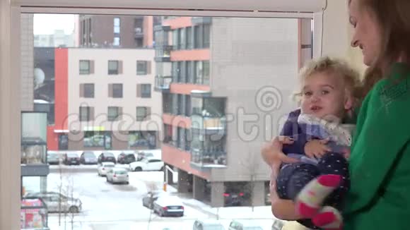 慈爱的母亲把淘气的女儿手放在窗边降雪视频的预览图