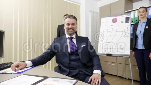 在繁忙的办公室里和他的两位同事一起工作的成功商人微笑的肖像视频的预览图