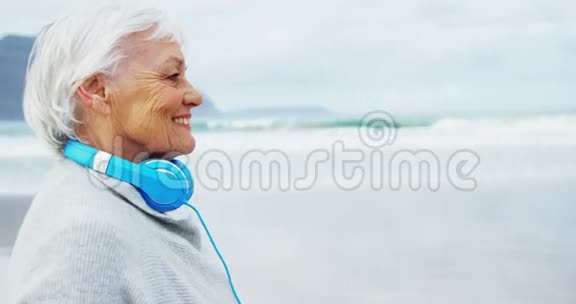 在沙滩上散步时戴着耳机的老妇人视频的预览图