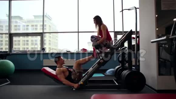 一个男性运动员做腿部按压运动的侧视在健身房锻炼一个运动的女人坐在媒体上视频的预览图