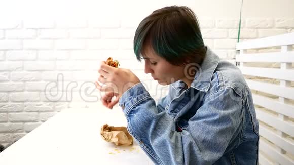女人吃三明治坐在咖啡馆的窗户附近视频的预览图