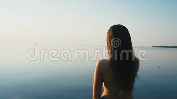 美丽的年轻女子在日落时用她的智能手机在海边度假慢动作视频的预览图