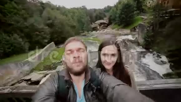 一对可爱的夫妇正站在一座木桥上在瀑布上摆姿势自拍视频的预览图