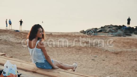 漂亮的女人坐在沙滩上看起来很开心视频的预览图