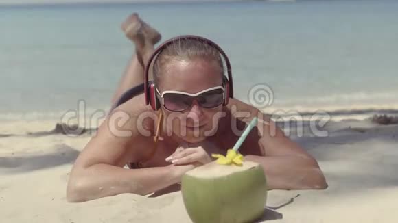 戴着耳机的女孩躺在海滩上看椰子视频的预览图