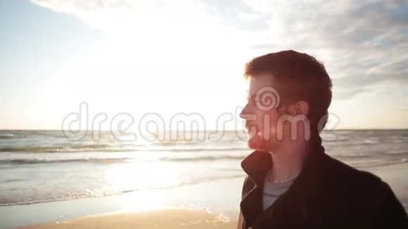 一位身穿黑色外套的黑发青年站在海边欣赏日落视频的预览图
