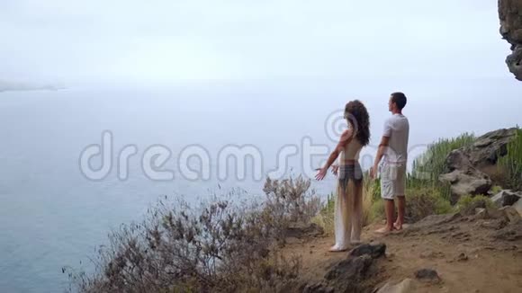 一男一女站在俯瞰大海的悬崖边上举起双手吸气视频的预览图