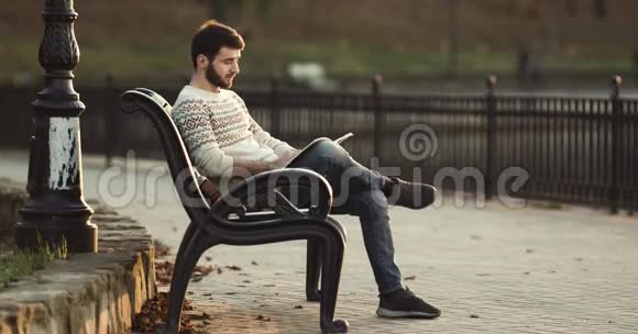 年轻人坐在长凳上在公园看书视频的预览图