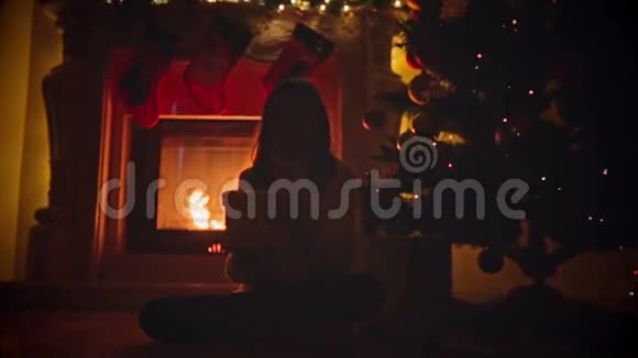 快乐女孩坐在壁炉前的地板上打开装有圣诞礼物的盒子视频的预览图