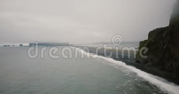 雾天黑火山海滩的鸟瞰图成群结队的游客在海上的灰烬岸上散步视频的预览图