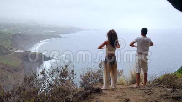 一男一女站在俯瞰大海的悬崖边上举起双手吸气视频的预览图