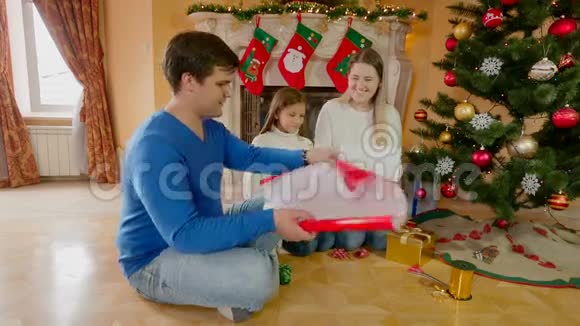 幸福的一家人坐在地板上用纸包装圣诞礼物用丝带装饰视频的预览图