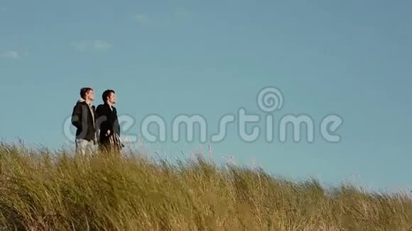 在大风天两个年轻人站在高高的草地上朝同一个方向看视频的预览图