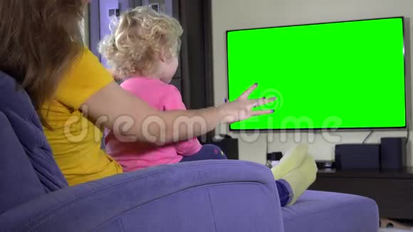 年轻的母亲和她的女儿女孩在沙发上放松看电视绿色屏幕视频的预览图