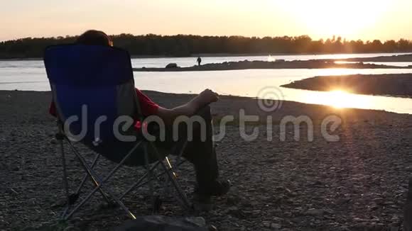 一个人不在海滩上休息坐在折叠椅上把脚踩在腿上享受日落慢动作视频的预览图