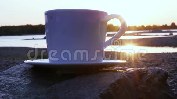 夕阳与阳光躲在岩石上的一杯热茶后面特写镜头slowmotion1920x1080高清视频的预览图