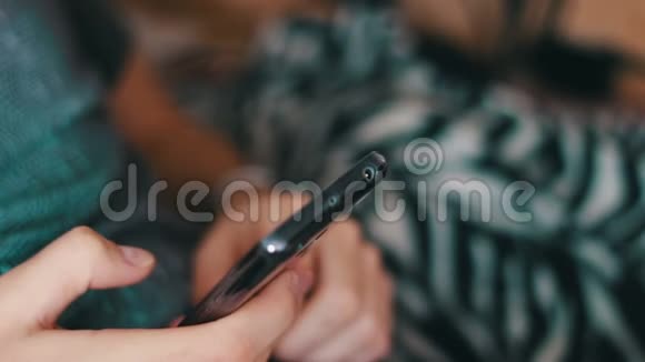 穿T恤和短裤的男人躺在沙发上手里拿着一部智能手机视频的预览图